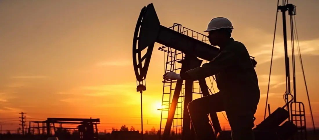 Oil pumpjack and engineer silhouetted at sunset