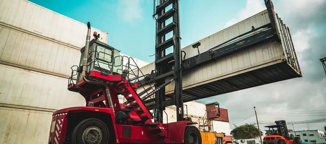 Container handler lifting a container beside rail wagons in a terminal