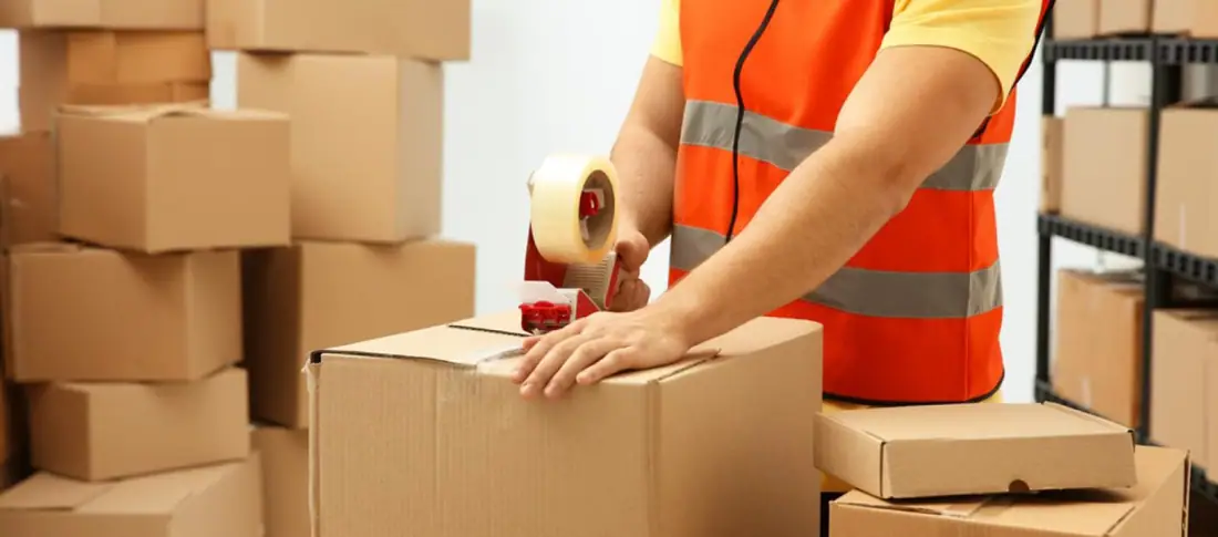 Packer sealing cardboard boxes in a warehouse